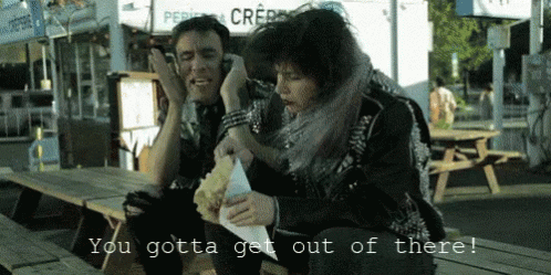 A Man And A Woman Sitting At A Picnic Table With The Words You Gotta Get Out Of There On The Bottom GIF