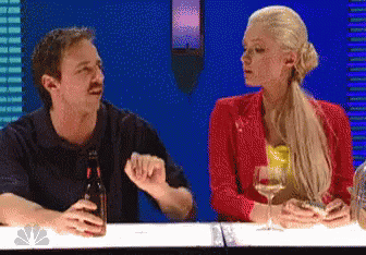 A Man And A Woman Sitting At A Table With A Bottle Of Beer And A Glass Of Wine GIF