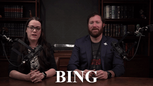 A Man And A Woman Sitting In Front Of A Microphone With A Sign That Says 80 % Bing GIF