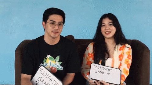 A Man And A Woman Sitting On A Couch Holding Up Signs That Say Telepathy Game GIF