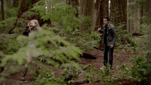 A Man And A Woman Standing In A Forest GIF