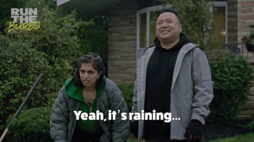 A Man And A Woman Standing In Front Of A House With Yeah It 'S Raining Written Below Them GIF