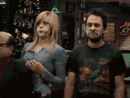 A Man And A Woman Standing Next To Each Other In Front Of A Bar GIF