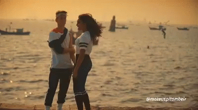 A Man And A Woman Standing Next To Each Other In Front Of The Ocean GIF