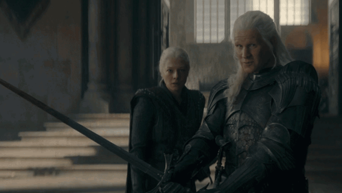 A Man And A Woman Standing Next To Each Other With Swords GIF