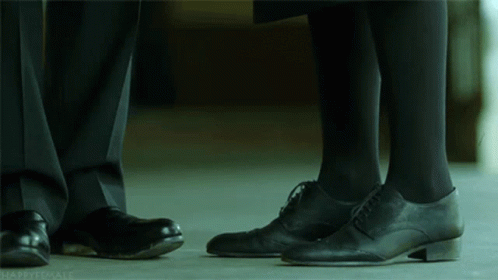 A Man And A Woman Standing Next To Each Other With Their Feet Touching GIF