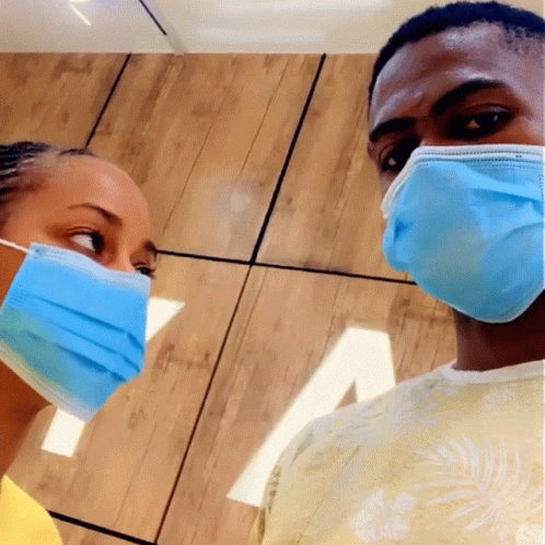 A Man And A Woman Wearing Blue Face Masks Looking At Each Other GIF