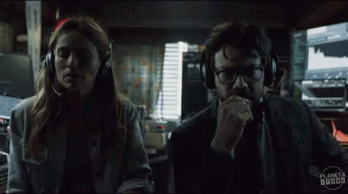 A Man And A Woman Wearing Headphones Are Looking At Each Other In A Dark Room . GIF