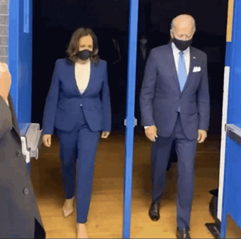 A Man And A Woman Wearing Masks Are Walking Out Of A Doorway . GIF