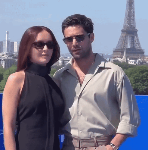 A Man And A Woman Wearing Sunglasses Pose In Front Of The Eiffel Tower GIF