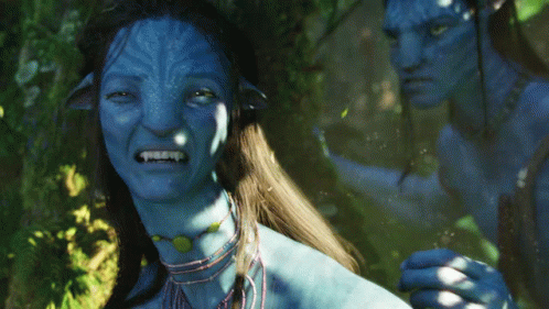 A Man And A Woman With Blue Faces Are Standing In A Forest GIF