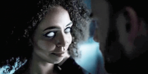 A Man And A Woman With White Eyes Are Looking At Each Other In A Dark Room . GIF