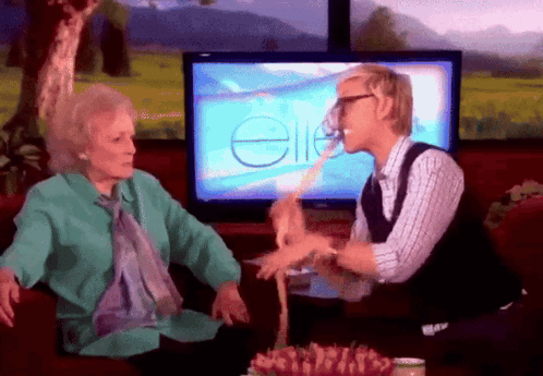 A Man And An Older Woman Are Sitting In Front Of A Television Screen With The Word Ellen On It GIF