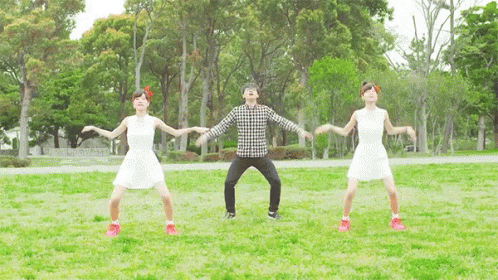 A Man And Two Women Are Dancing In A Park With Trees In The Background GIF