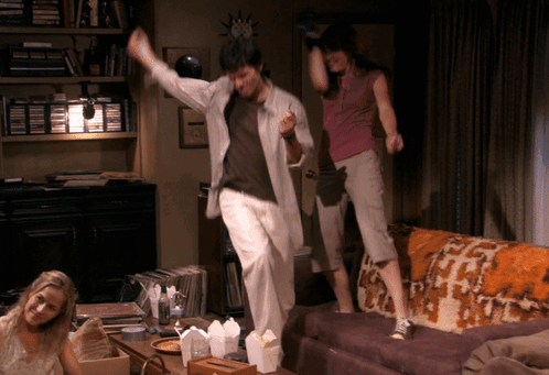 A Man And Two Women Are Jumping On A Couch GIF