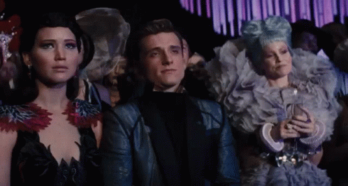 A Man And Two Women Are Sitting In A Crowd Looking At Something GIF
