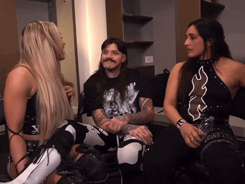 A Man And Two Women Are Sitting In A Room And The Man Has A Tattoo On His Arm That Says ' X ' On It GIF
