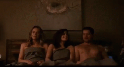 A Man And Two Women Are Sitting On A Bed Without Shirts . GIF