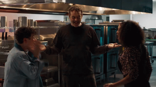 A Man And Two Women Are Standing In A Kitchen And The Man Is Smiling GIF
