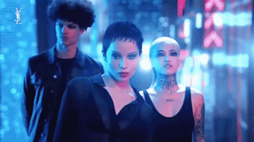 A Man And Two Women Are Standing Next To Each Other In A Dark Room With Neon Lights Behind Them . GIF