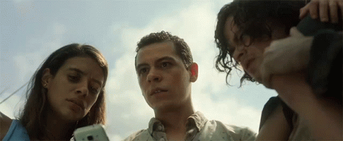 A Man And Two Women Look At A Cell Phone Together GIF