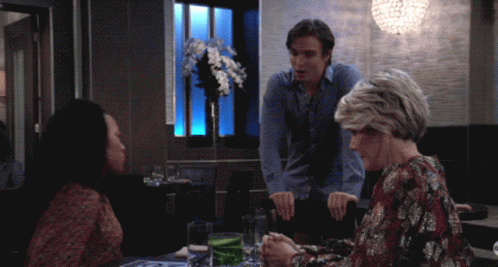 A Man And Two Women Sit At A Table In A Restaurant Talking GIF