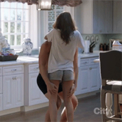 A Man And Woman Are Dancing In A Kitchen With A City Logo On The Bottom GIF