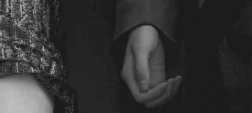 A Man And Woman Are Holding Hands In A Black And White Photo . GIF
