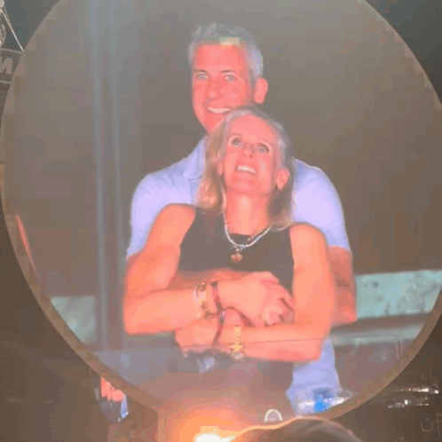 A Man And Woman Are Hugging Each Other In Front Of A Sign That Says M GIF