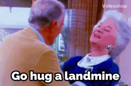 A Man And Woman Are Hugging With The Words Go Hug A Landmine In The Foreground GIF