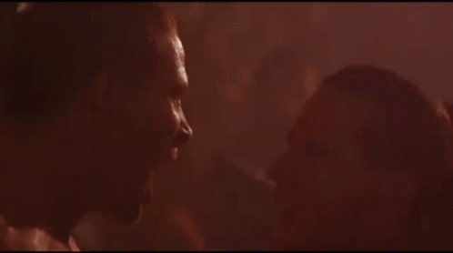 A Man And Woman Are Kissing In A Dark Room In A Movie . GIF