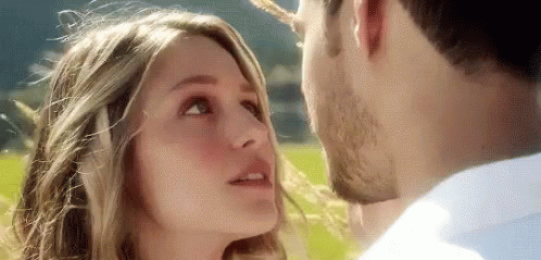 A Man And Woman Are Kissing In A Field . GIF