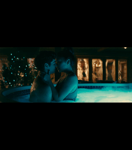 A Man And Woman Are Kissing In A Hot Tub At Night GIF
