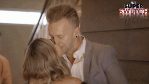 A Man And Woman Are Kissing In Front Of A Sign That Says Super Switch GIF
