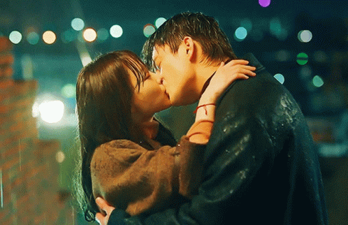 A Man And Woman Are Kissing In The Rain At Night GIF