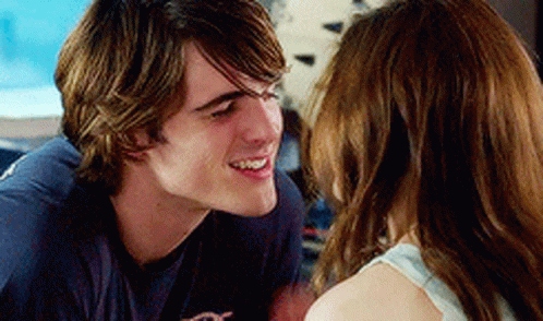 A Man And Woman Are Looking At Each Other And Smiling . GIF