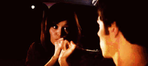 A Man And Woman Are Looking At Each Other In A Dark Room GIF