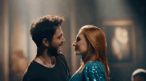 A Man And Woman Are Looking At Each Other In A Dark Room . GIF