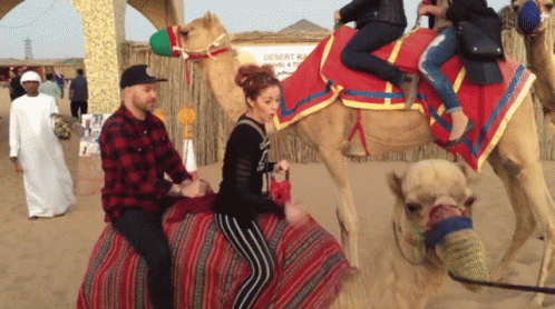 A Man And Woman Are Riding A Camel In The Desert GIF