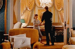 A Man And Woman Are Shaking Hands In A Living Room . GIF