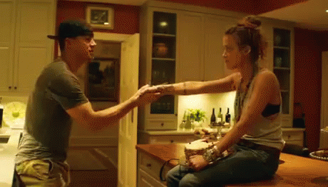 A Man And Woman Are Sitting At A Counter In A Kitchen Holding Hands . GIF