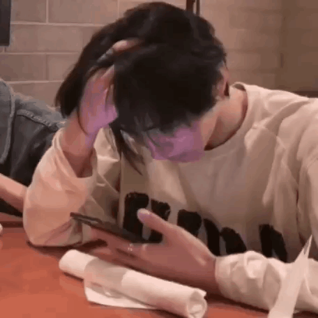 A Man And Woman Are Sitting At A Table Looking At A Cell Phone . GIF