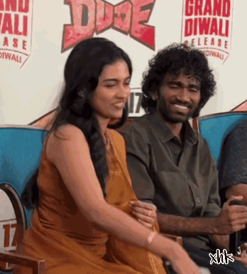 A Man And Woman Are Sitting In Front Of A Sign That Says Grand Diwali Release GIF