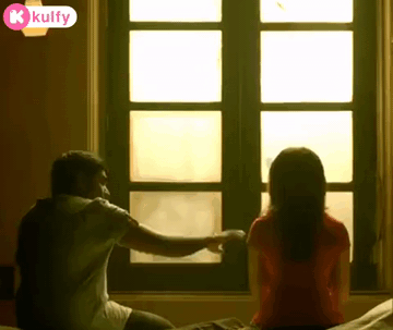 A Man And Woman Are Sitting On A Bed Looking Out A Window . GIF