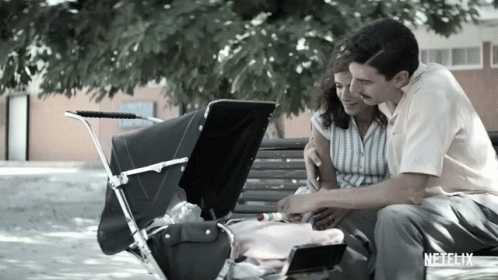 A Man And Woman Are Sitting On A Bench With A Baby In A Stroller And A Netflix Logo In The Corner GIF