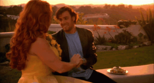 A Man And Woman Are Sitting On A Bench With A Plate Of Food In Front Of Them GIF
