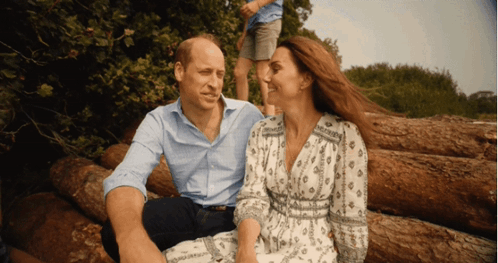 A Man And Woman Are Sitting On A Pile Of Logs GIF