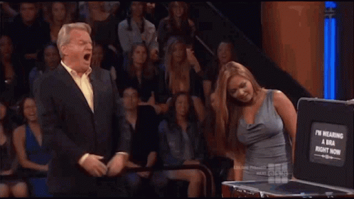 A Man And Woman Are Standing In Front Of A Briefcase That Says I 'M Wearing A Bra GIF