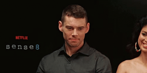 A Man And Woman Are Standing In Front Of A Sign That Says Sense 8 GIF