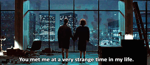A Man And Woman Are Standing In Front Of A Window With The Words You Met Me At A Very Strange Time In My Life Below Them GIF